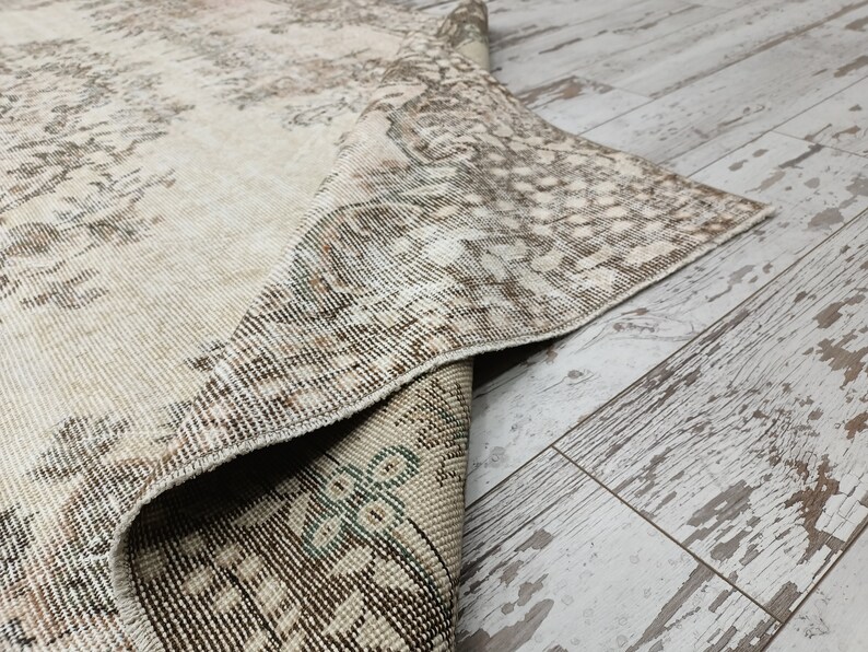 May include: A close-up of a beige and brown patterned rug with a frayed edge. The rug is folded over and the underside is visible.