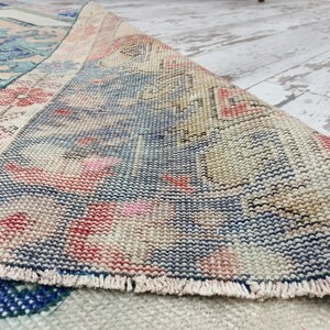 K&ouml;nnte beinhalten: Nahaufnahme des Randes eines Vintage-Teppichs mit einem gewebten Muster in Blaut&ouml;nen, Rosa und Beige. Der Teppich hat einen Fransenrand.
