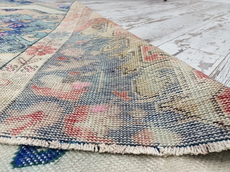 K&ouml;nnte beinhalten: Nahaufnahme des Randes eines Vintage-Teppichs mit einem gewebten Muster in Blaut&ouml;nen, Rosa und Beige. Der Teppich hat einen Fransenrand.