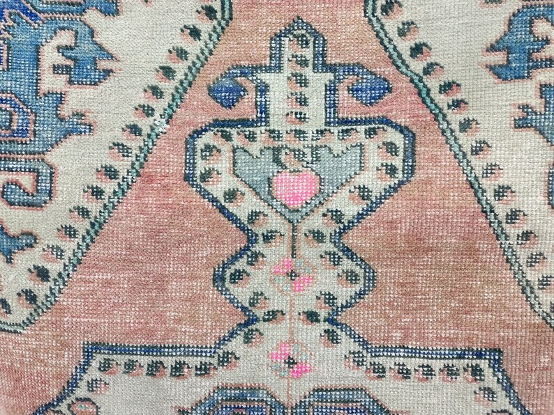Pode incluir: Close-up de um tapete rosa e azul com detalhes intrincados. O tapete tem um design tradicional com um motivo central e padr&otilde;es repetidos.