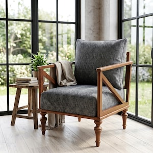 May include: A grey upholstered armchair with a wooden frame and legs. A matching grey cushion and a beige throw blanket are on the chair. A small wooden side table with books and a potted plant sits nearby.