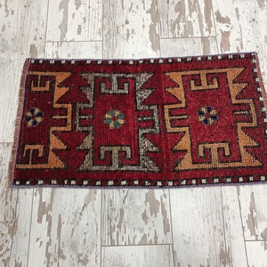 May include: A red, orange, and black patterned rug with a geometric design. The rug has a fringe border and is made of wool.