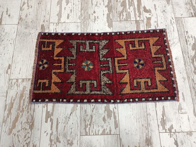 May include: A red, orange, and black patterned rug with a geometric design. The rug has a fringe border and is made of wool.