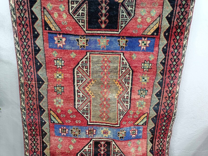 May include: A vintage red, blue, and green rug with a geometric pattern. The rug has a central medallion with a repeating pattern of stars and diamonds.