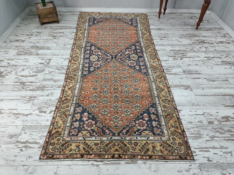 May include: A vintage runner rug with a floral pattern in shades of orange, blue, and cream. The rug has a border with a geometric design.