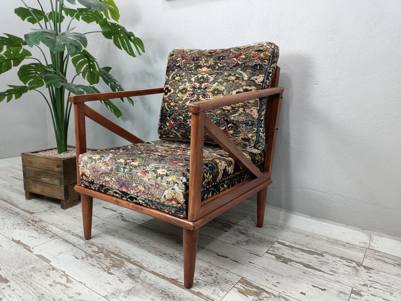 May include: A wooden armchair with a patterned fabric upholstery. The chair has a unique X-shaped design on the back and arms. The fabric is a mix of brown, green, and red colors.