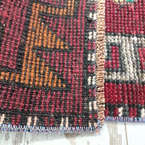 May include: Close-up of a red, black, and orange patterned rug with a fringe edge. The rug is woven with a variety of textures and colors.