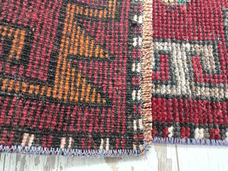 May include: Close-up of a red, black, and orange patterned rug with a fringe edge. The rug is woven with a variety of textures and colors.