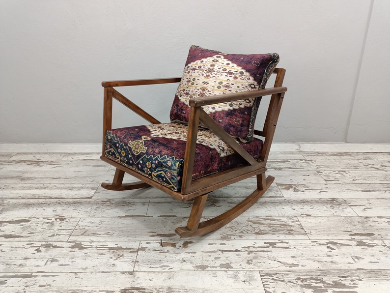 May include: Wooden rocking chair with a patterned cushion and backrest. The cushion and backrest feature a burgundy, cream, and navy blue design. The chair has a dark brown wooden frame and is set on a white and gray wooden floor.