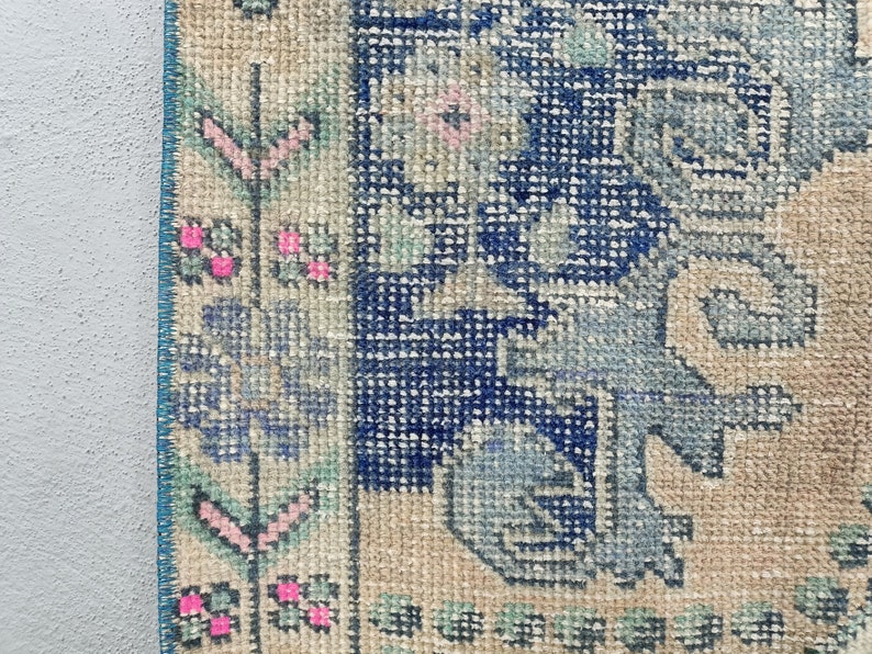 K&ouml;nnte beinhalten: Nahaufnahme eines Vintage-Teppichs mit einem blauen und wei&szlig;en Blumenmuster. Der Teppich hat einen hellbeigen Hintergrund und einen blauen Rand.