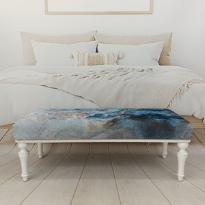 Puede incluir: Banco de madera blanco con patas torneadas y una tapa de tela con estampado azul y gris. El banco est&aacute; en un dormitorio.