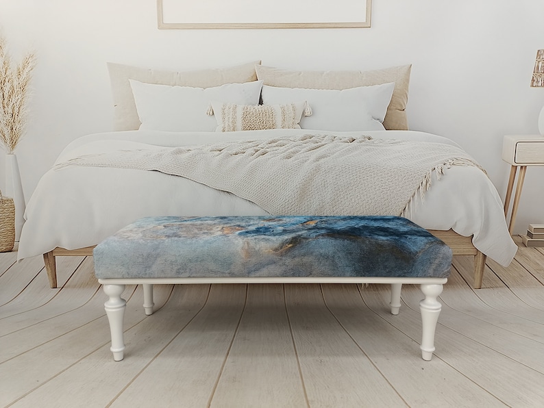 Puede incluir: Banco de madera blanco con patas torneadas y una tapa de tela con estampado azul y gris. El banco est&aacute; en un dormitorio.