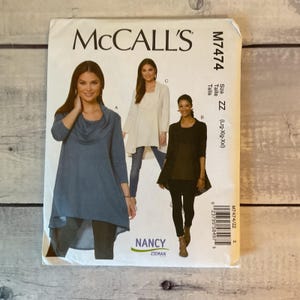 May include: McCall's sewing pattern M7474, size ZZ (Lrg-Xlg-Xxl), featuring designs for a tunic with a cowl neckline and a long cardigan. The envelope displays three variations of the garment in blue, white, and black, with Nancy Zieman branding.
