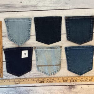 Pode incluir: Seis bolsos de ganga em v&aacute;rios tons de azul, desde lavagem clara a &iacute;ndigo escuro, dispostos em duas filas. Uma r&eacute;gua de madeira &agrave; esquerda mostra uma altura de 15 cm e uma r&eacute;gua horizontal na parte inferior mede 53 cm de comprimento.