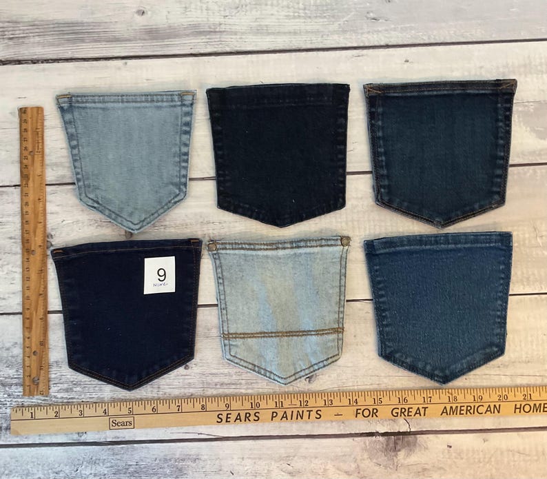 Pode incluir: Seis bolsos de ganga em v&aacute;rios tons de azul, desde lavagem clara a &iacute;ndigo escuro, dispostos em duas filas. Uma r&eacute;gua de madeira &agrave; esquerda mostra uma altura de 15 cm e uma r&eacute;gua horizontal na parte inferior mede 53 cm de comprimento.