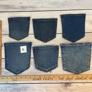 Pode incluir: Seis bolsos de ganga azul separados de v&aacute;rios tons e tamanhos dispostos em duas filas. Uma r&eacute;gua de madeira &agrave; esquerda mostra uma altura de cerca de 16,5 cm para o bolso inferior esquerdo, e uma r&eacute;gua horizontal na base mede 56 cm.