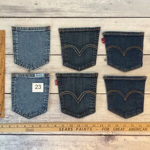 Puede incluir: Seis bolsillos de mezclilla separados dispuestos en dos filas. Los bolsillos var&iacute;an en tonos azules, cuatro con un patr&oacute;n de costura arqueado caracter&iacute;stico y etiquetas rojas. Un bolsillo tiene una etiqueta azul claro de Bill Blass y el n&uacute;mero 23.