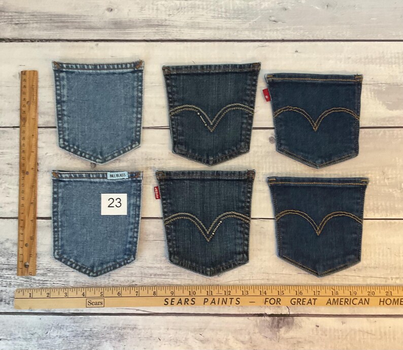 Puede incluir: Seis bolsillos de mezclilla separados dispuestos en dos filas. Los bolsillos var&iacute;an en tonos azules, cuatro con un patr&oacute;n de costura arqueado caracter&iacute;stico y etiquetas rojas. Un bolsillo tiene una etiqueta azul claro de Bill Blass y el n&uacute;mero 23.
