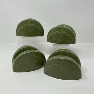 May include: A set of four olive green semi-circular napkin holders. Each piece features a smooth, glossy finish and a raised, horizontal decorative band across the center with a repeating geometric link pattern molded into the surface.