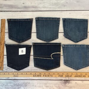 Pode incluir: Seis bolsos de ganga azul sortidos dispostos em duas filas. Uma r&eacute;gua de madeira &agrave; esquerda mostra uma altura de aproximadamente 12,7 cm, e uma r&eacute;gua Sears Paints na parte inferior mostra uma largura de aproximadamente 55,9 cm. Um bolso tem uma etiqueta branca com o n&uacute;mero 8.