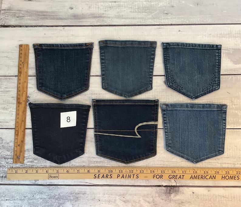 Pode incluir: Seis bolsos de ganga azul sortidos dispostos em duas filas. Uma r&eacute;gua de madeira &agrave; esquerda mostra uma altura de aproximadamente 12,7 cm, e uma r&eacute;gua Sears Paints na parte inferior mostra uma largura de aproximadamente 55,9 cm. Um bolso tem uma etiqueta branca com o n&uacute;mero 8.