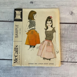 May include: Vintage McCall's printed pattern for Misses' and Junior short aprons. The cover features illustrations of women wearing aprons with pockets. The pattern is labeled "Sample" and "One Size".