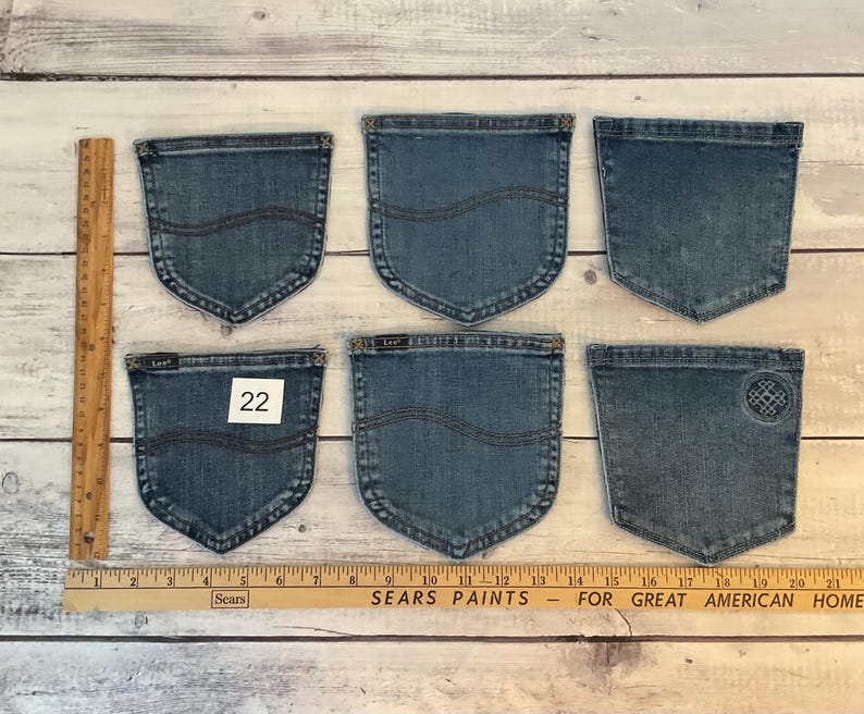 Puede incluir: Seis bolsillos de mezclilla azul dispuestos en dos filas, con una regla de madera que muestra una longitud de 53 cm. Los bolsillos tienen detalles de costura, uno tiene una etiqueta Lee, uno un dise&ntilde;o bordado circular y uno una etiqueta con el 22.