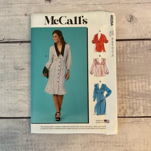 May include: McCall's sewing pattern M8284 featuring a woman's dress with a black collar and polka dots. The pattern includes multiple view options with simple instructions. The size is A5 (6-8-10-12-14). Designed and printed in the USA.