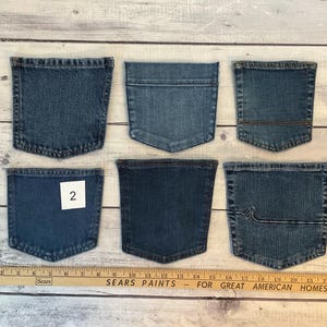 Pode incluir: Seis bolsos de ganga azul sortidos dispostos em duas filas. Uma r&eacute;gua de madeira &agrave; esquerda mostra uma altura de 15 cm, e uma r&eacute;gua horizontal na parte inferior mostra uma largura de 58 cm. Um bolso apresenta uma etiqueta quadrada branca com o n&uacute;mero 2.