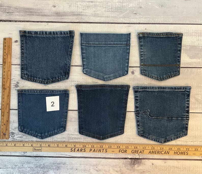 Pode incluir: Seis bolsos de ganga azul sortidos dispostos em duas filas. Uma r&eacute;gua de madeira &agrave; esquerda mostra uma altura de 15 cm, e uma r&eacute;gua horizontal na parte inferior mostra uma largura de 58 cm. Um bolso apresenta uma etiqueta quadrada branca com o n&uacute;mero 2.