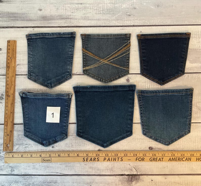 Pode incluir: Seis bolsos de ganga em v&aacute;rios tons de azul dispostos numa superf&iacute;cie, com um bolso etiquetado com o n&uacute;mero 1. Uma r&eacute;gua de madeira est&aacute; posicionada verticalmente &agrave; esquerda e horizontalmente na parte inferior, mostrando medidas em polegadas.