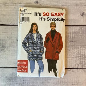 May include: A Simplicity sewing pattern envelope 8467 featuring illustrations of two jackets. One jacket is blue with a white reindeer and snowflake pattern, and the other is solid red with black trim. The text reads It's SO EASY it's Simplicity.