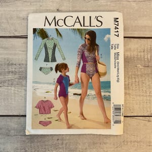 May include: McCall's M7417 sewing pattern featuring swimwear designs for women and girls. The pattern includes illustrations of various swimsuit styles, including a long-sleeved top and high-waisted bottoms, with size options from small to extra-large.