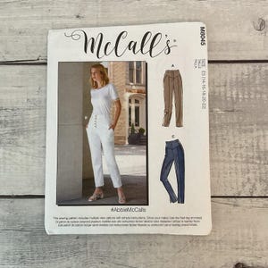 May include: A McCall's sewing pattern featuring a woman wearing white pants and a white top. The pattern includes multiple view options with simple instructions. The pattern size is E5 (14-16-18-20-22).