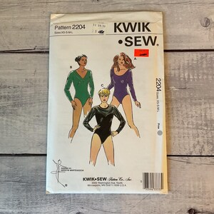 May include: A Kwik Sew pattern envelope 2204 for leotards in sizes XS-S-M-L. The front displays illustrations of three long-sleeved leotards in green, purple, and black, with a red sale sticker and the company name printed at the top.