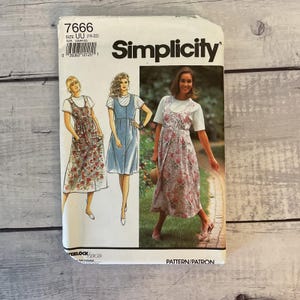 May include: Simplicity sewing pattern 7666 for a sleeveless dress with a button-front closure. The envelope features illustrations and a photograph of the dress worn over a short-sleeved t-shirt, showcasing floral and solid fabric options.