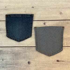 Pode incluir: Dois bolsos de ganga separados, um mostrando o exterior azul escuro com costuras cor de cobre e o outro mostrando o forro interior cinzento claro com costuras vis&iacute;veis, ambos com uma forma cl&aacute;ssica de cinco lados e cantos arredondados.