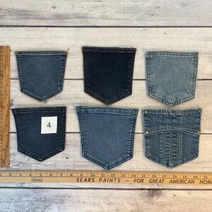 Pode incluir: Seis bolsos de ganga em v&aacute;rios tons de azul, dispostos em duas filas. Um bolso apresenta uma etiqueta quadrada branca com o n&uacute;mero 4. Uma r&eacute;gua de madeira est&aacute; colocada verticalmente &agrave; esquerda e horizontalmente na base, mostrando medidas em cm.