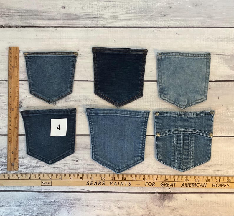 Pode incluir: Seis bolsos de ganga em v&aacute;rios tons de azul, dispostos em duas filas. Um bolso apresenta uma etiqueta quadrada branca com o n&uacute;mero 4. Uma r&eacute;gua de madeira est&aacute; colocada verticalmente &agrave; esquerda e horizontalmente na base, mostrando medidas em cm.