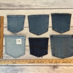 Pode incluir: Seis bolsos de ganga em v&aacute;rios tons de azul dispostos em duas filas. Uma r&eacute;gua de madeira est&aacute; colocada verticalmente &agrave; esquerda e horizontalmente na parte inferior, mostrando medidas em polegadas. Um bolso tem uma etiqueta quadrada branca com o n&uacute;mero 13.