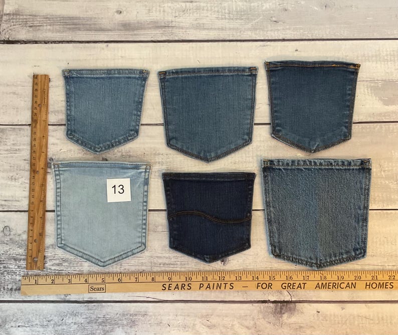 Pode incluir: Seis bolsos de ganga em v&aacute;rios tons de azul dispostos em duas filas. Uma r&eacute;gua de madeira est&aacute; colocada verticalmente &agrave; esquerda e horizontalmente na parte inferior, mostrando medidas em polegadas. Um bolso tem uma etiqueta quadrada branca com o n&uacute;mero 13.
