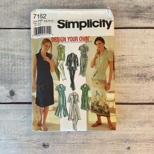 May include: A Simplicity sewing pattern packet, model 7162, featuring illustrations of various women's clothing designs. The packet includes the text "DESIGN YOUR OWN" and size information.