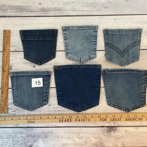 Puede incluir: Seis bolsillos de mezclilla variados en diferentes tonos de azul, desde claro hasta oscuro. Un bolsillo tiene una etiqueta blanca con el n&uacute;mero 15. Una regla de madera est&aacute; colocada vertical y horizontalmente para mostrar la escala en cent&iacute;metros.