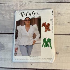 May include: A McCall's sewing pattern envelope featuring a woman wearing a white wrap top with large sleeves. The envelope includes illustrations of the top in different colors and styles. The text on the envelope includes the size range and the hashtag #MyrtleMcCalls.