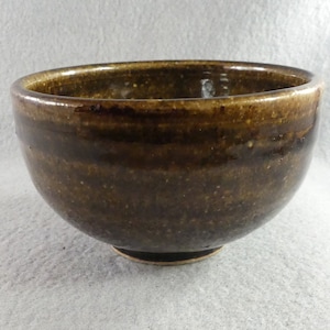 May include: A small, brown ceramic bowl with a speckled glaze. The bowl has a rounded shape and a slightly flared rim.