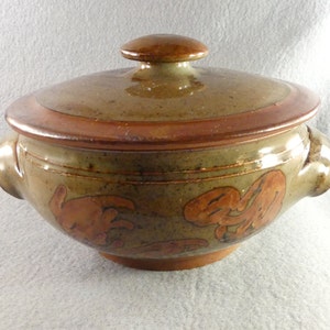 May include: A brown ceramic casserole dish with a lid. The dish has a speckled glaze and is decorated with brown and orange leaf designs. The lid has a brown knob.