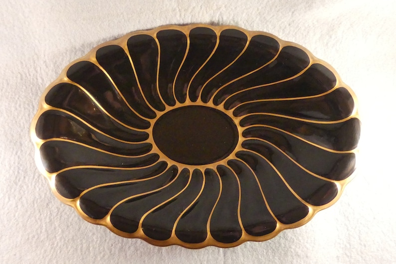 May include: A black and gold oval serving dish with a swirl design. The dish is made of ceramic and has a glossy finish.