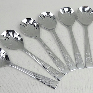 May include: Six silver spoons with ornate handles and a scalloped bowl. The spoons are arranged in a fan shape.