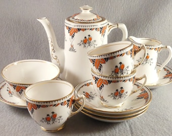 May include: A vintage tea set with a white background and orange and black floral design. The set includes a teapot, creamer, sugar bowl, and two teacups and saucers.