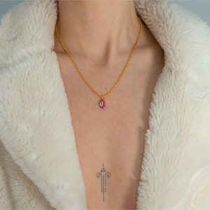 Könnte beinhalten: Eine goldene Kettenkette mit einem rosa-weißen Muschel-Anhänger. Die Kette wird von einer Person getragen, die eine weiße flauschige Jacke trägt.